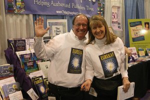 Two people holding up books at a book fair.
