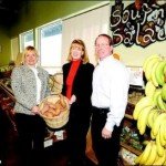 Three people standing in a store holding bananas.