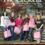 A group of women holding pink bags in front of a log house.