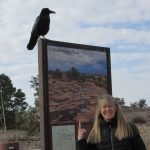 A woman standing next to a sign with a bird perched on top of it.