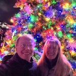 A man and woman standing in front of a christmas tree.